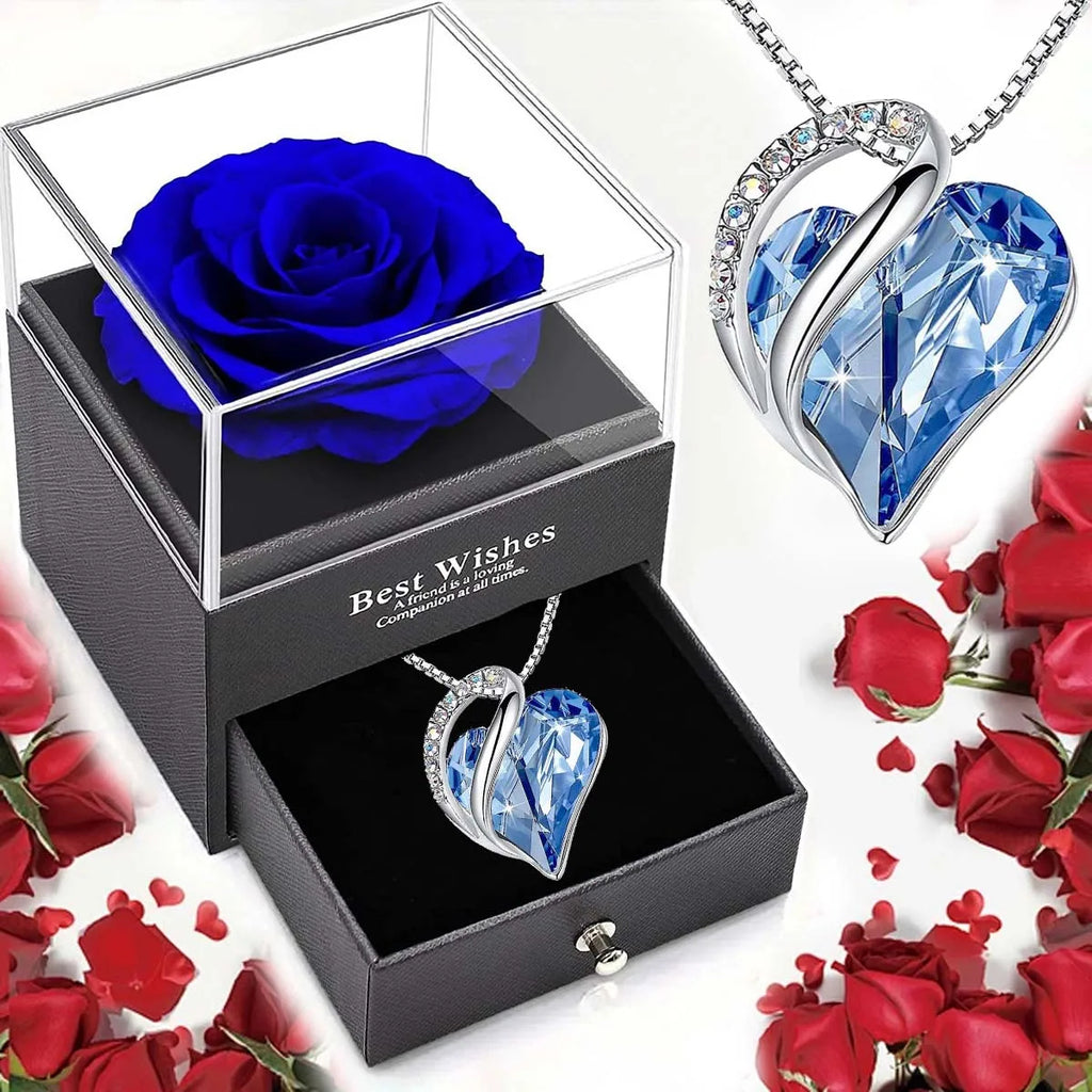 Blue rose in glass box with heart-shaped blue crystal pendant necklace, surrounded by red roses