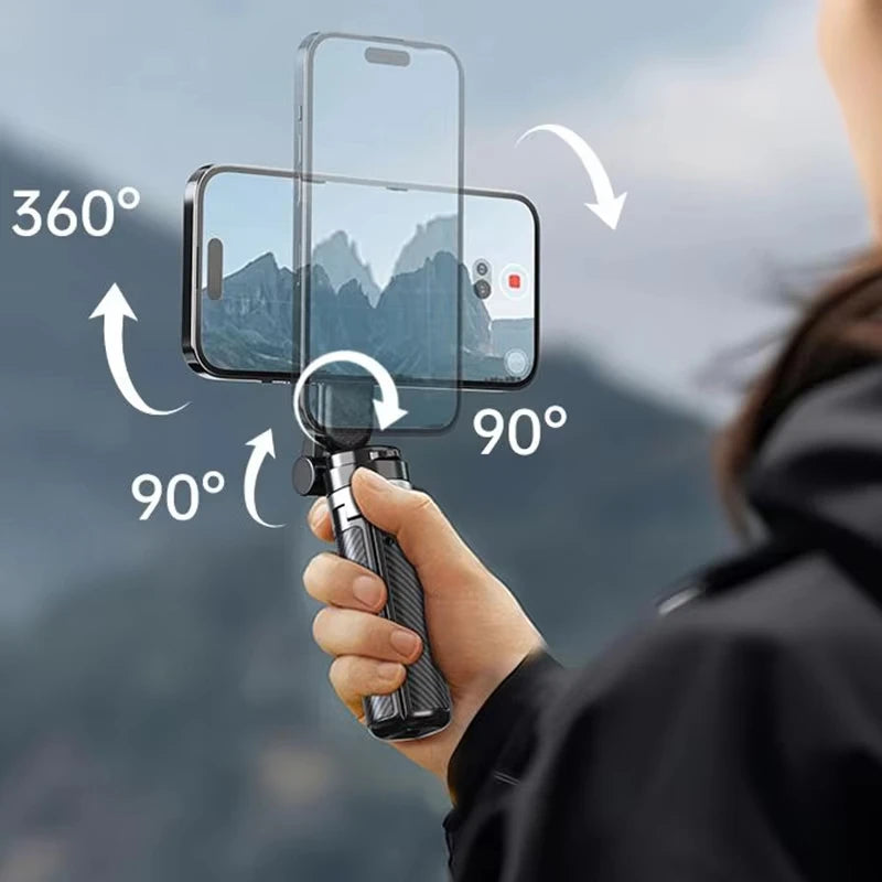 Hand holding a smartphone with a gimbal stabilizer, showing mountainous landscape through phone screen.