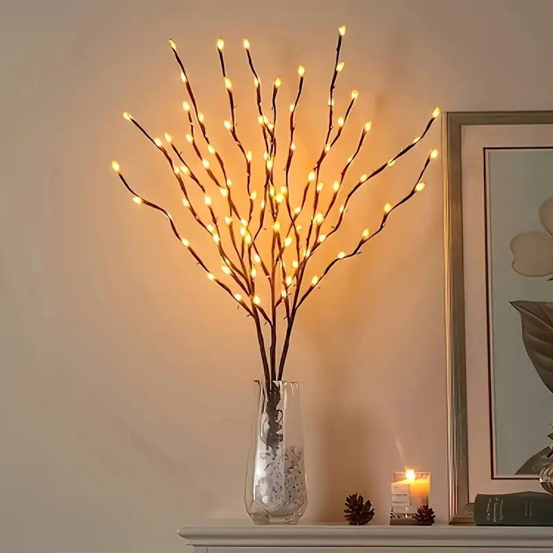 Decorative light branch in a vase on a shelf with a candle and framed picture in the background.