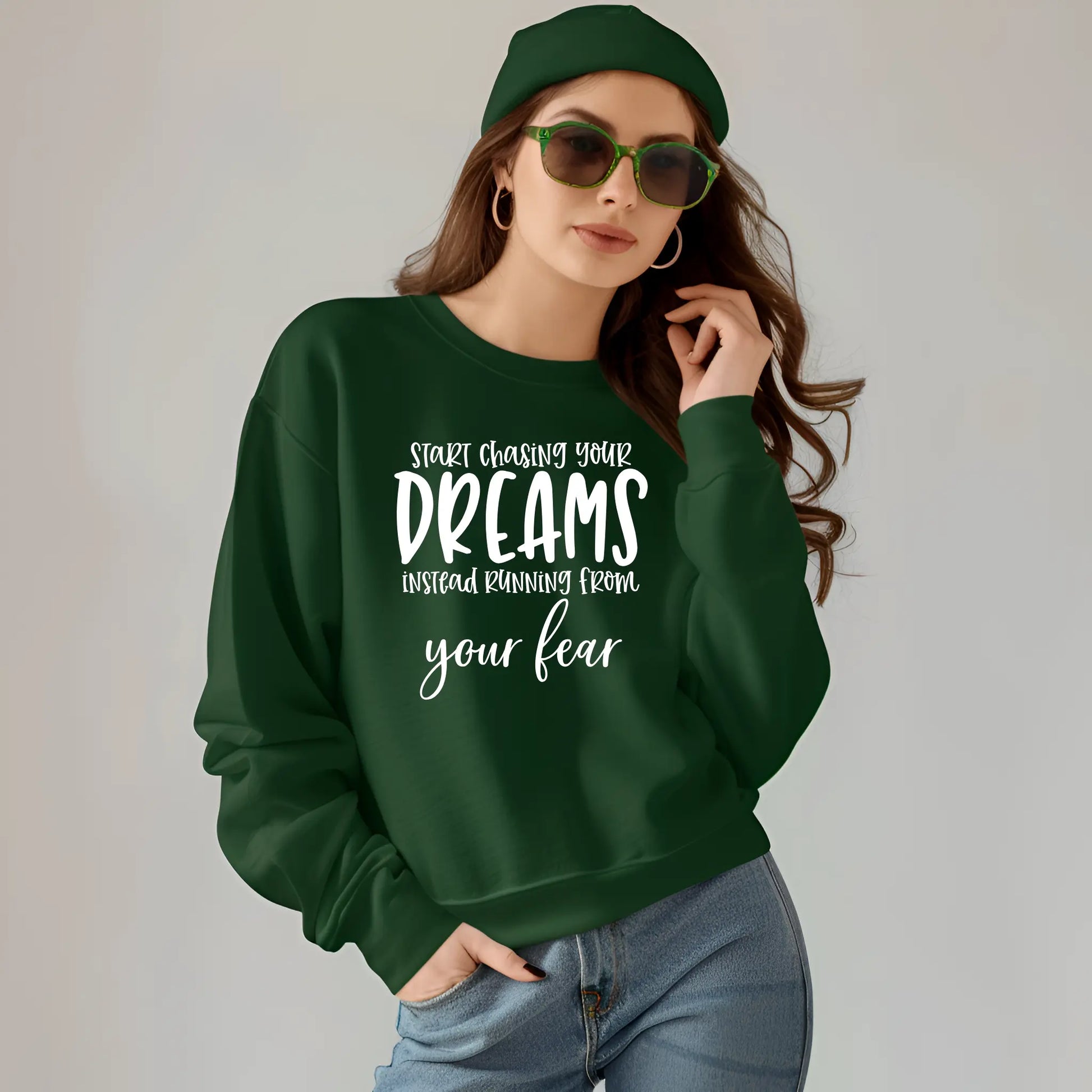 Woman wearing a green sweatshirt with motivational quote, sunglasses, and green cap on a plain background