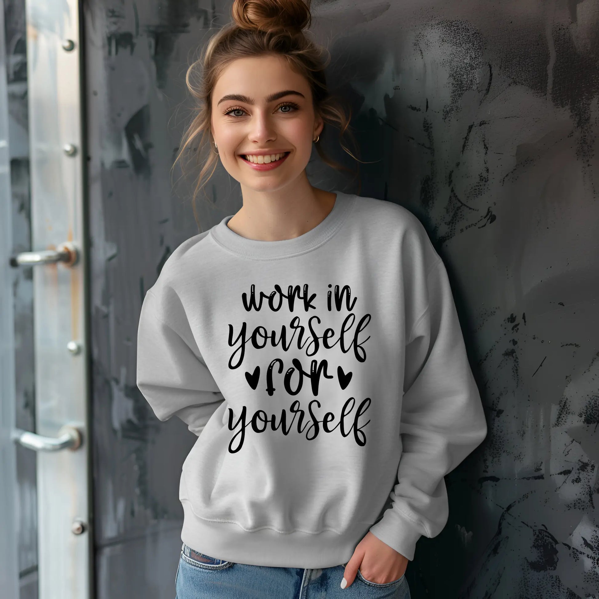 Woman wearing a gray sweatshirt with motivational text against a textured wall.