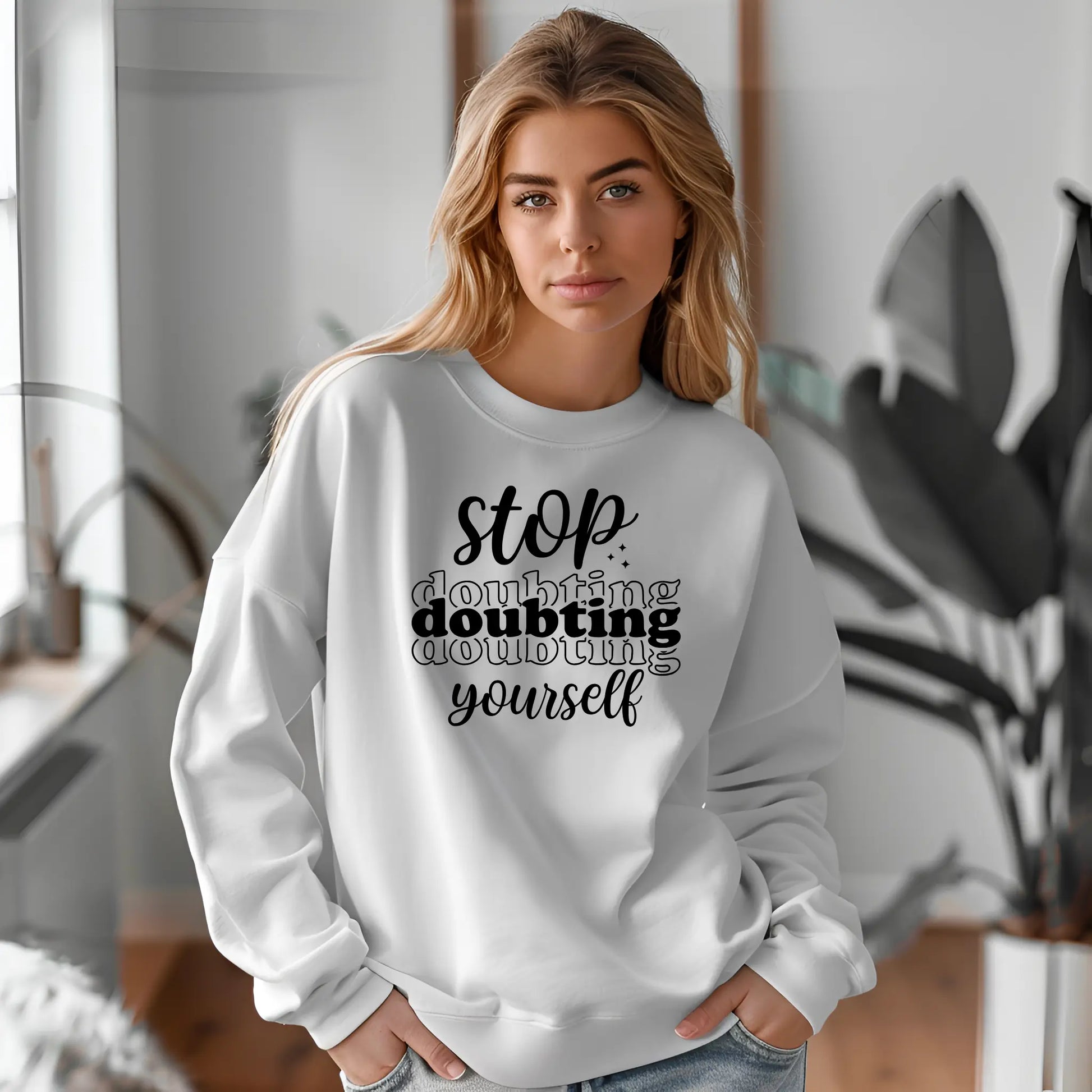 Woman wearing a white sweatshirt with motivational text in a modern indoor setting
