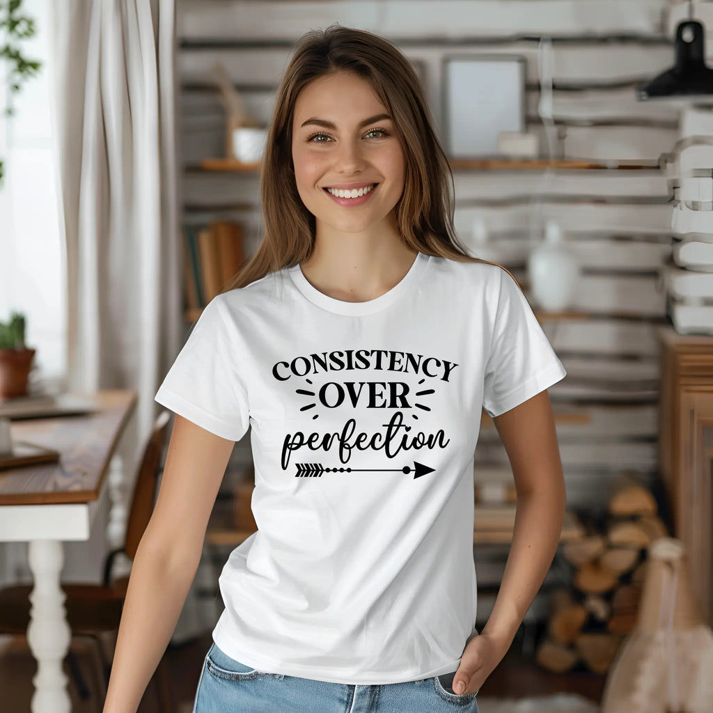 Woman wearing a white t-shirt with 'Consistency over perfection' text in a home setting
