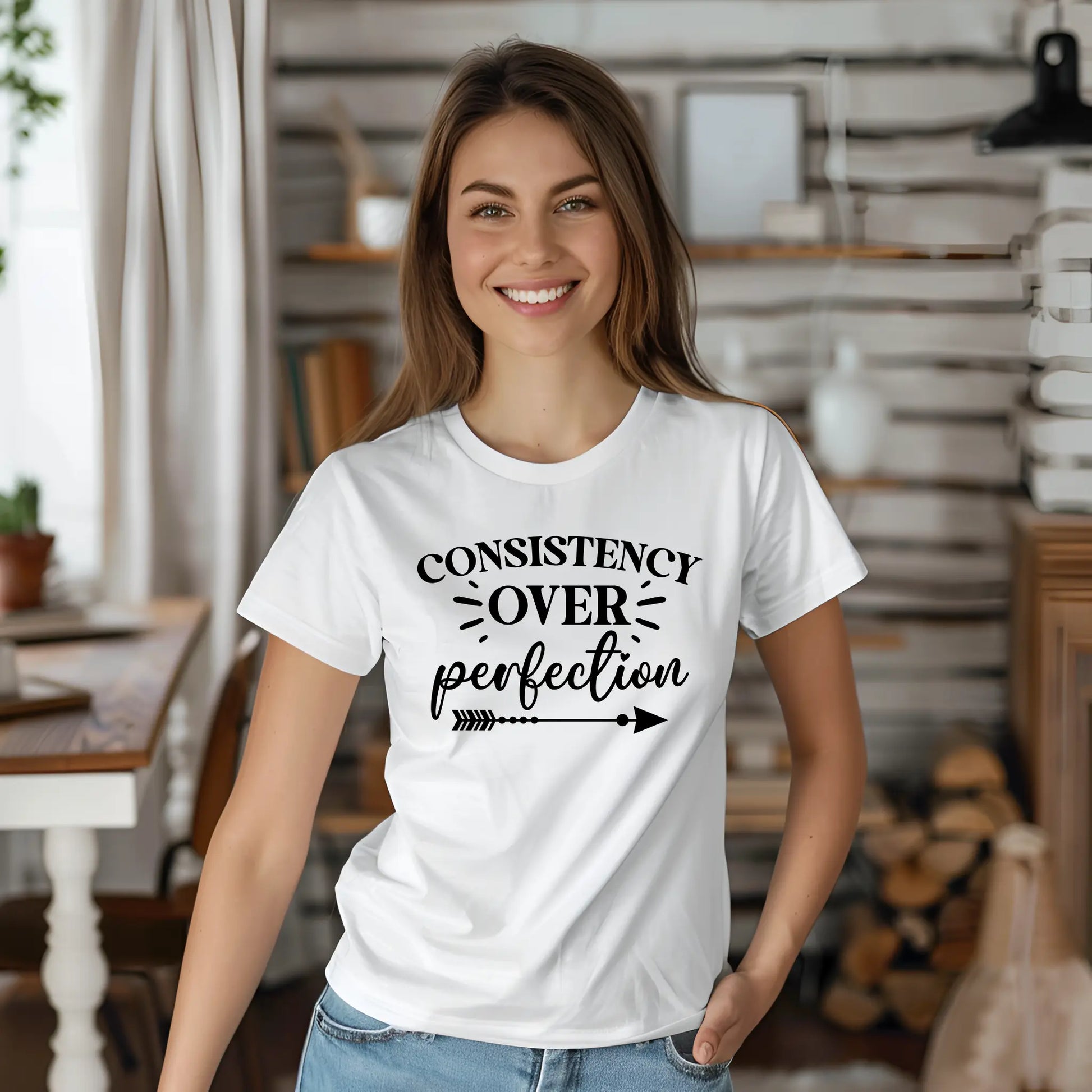 Woman wearing a white t-shirt with 'Consistency over perfection' text in a home setting