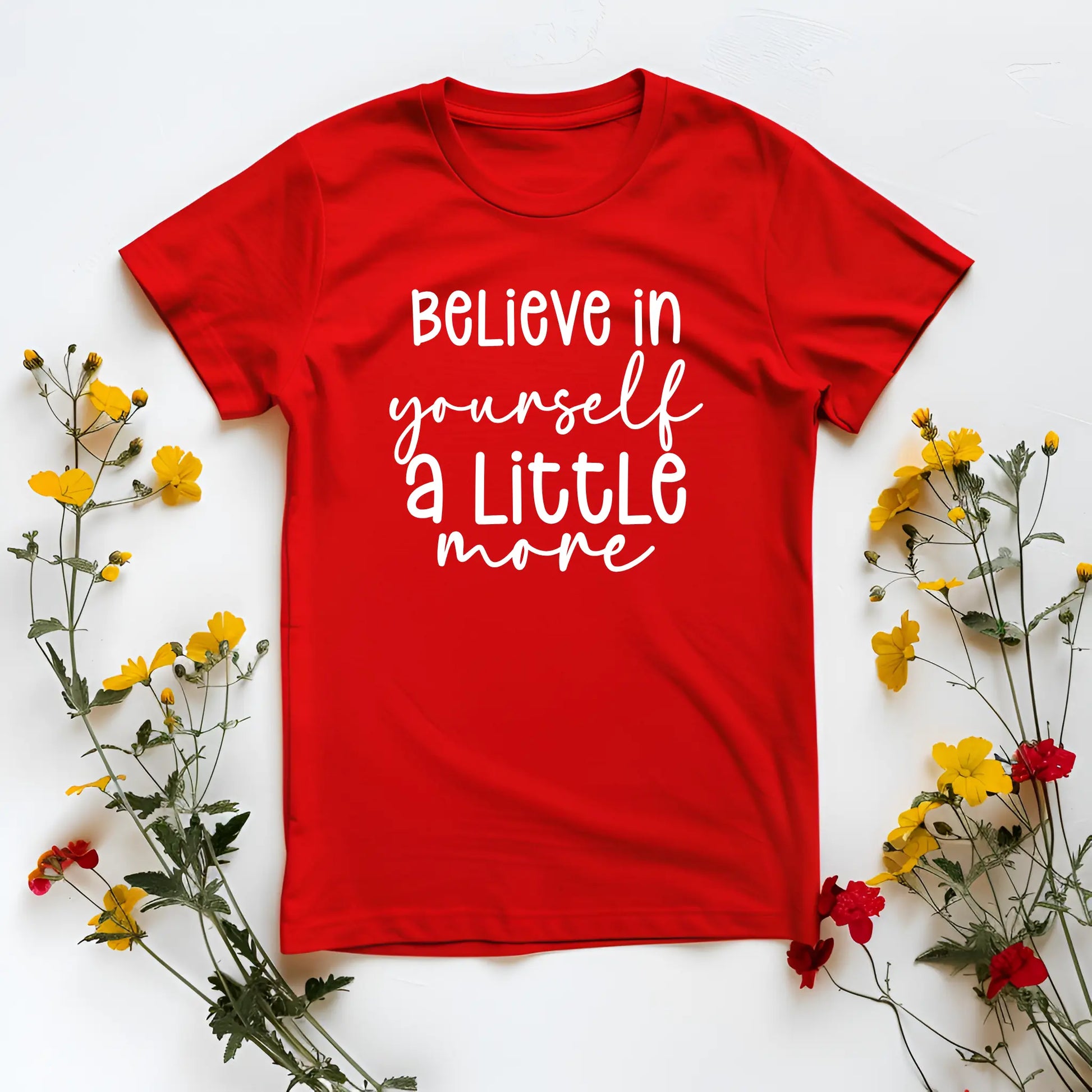 Red t-shirt with 'Believe in yourself a little more' text on a white background with flowers.