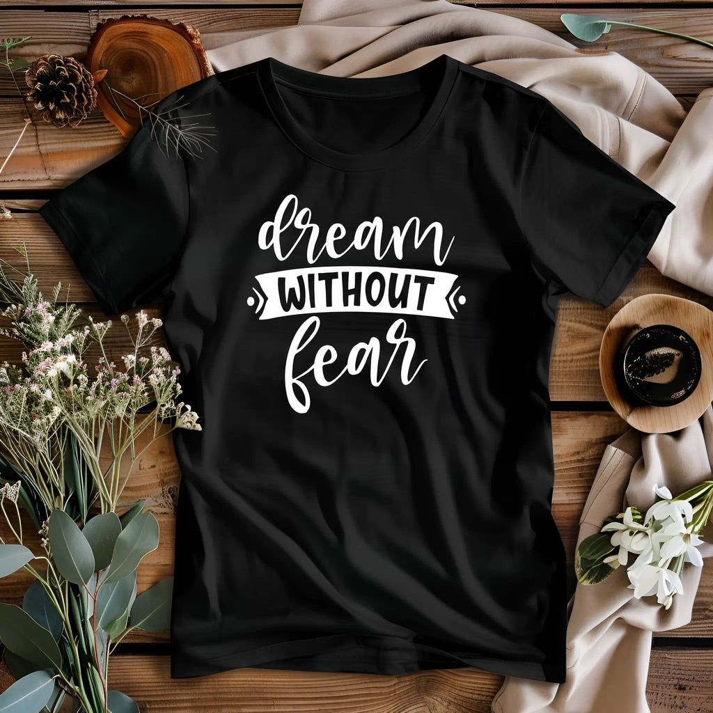 Black t-shirt with 'dream without fear' text on a wooden surface with decorative elements.