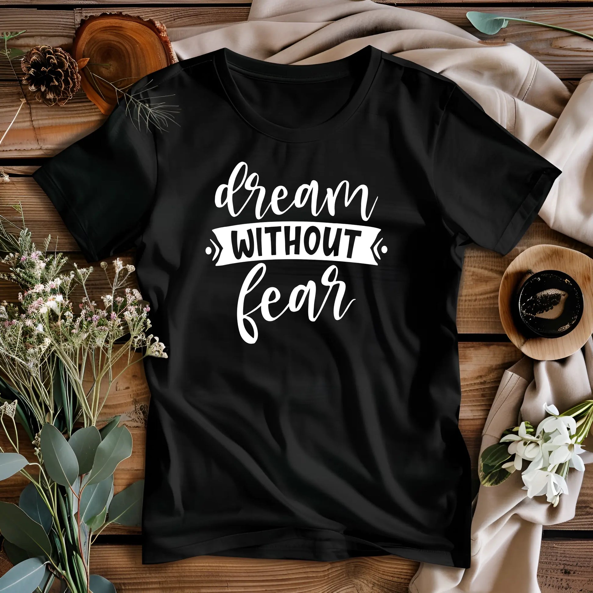 Black t-shirt with 'dream without fear' text on a wooden surface with decorative elements.