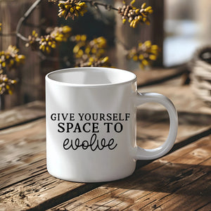 White mug with 'Give yourself space to evolve' text on a wooden surface with blurred natural background