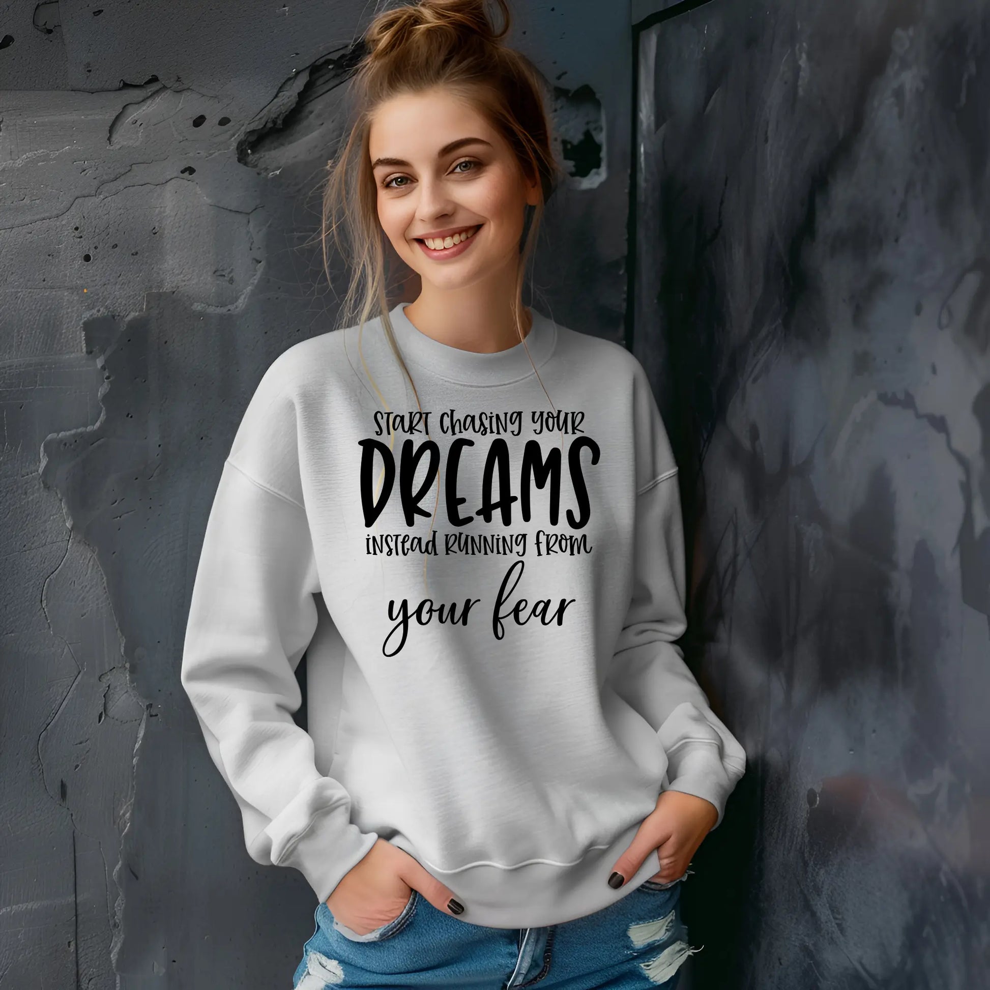 Woman wearing a gray sweatshirt with motivational text against a textured wall.