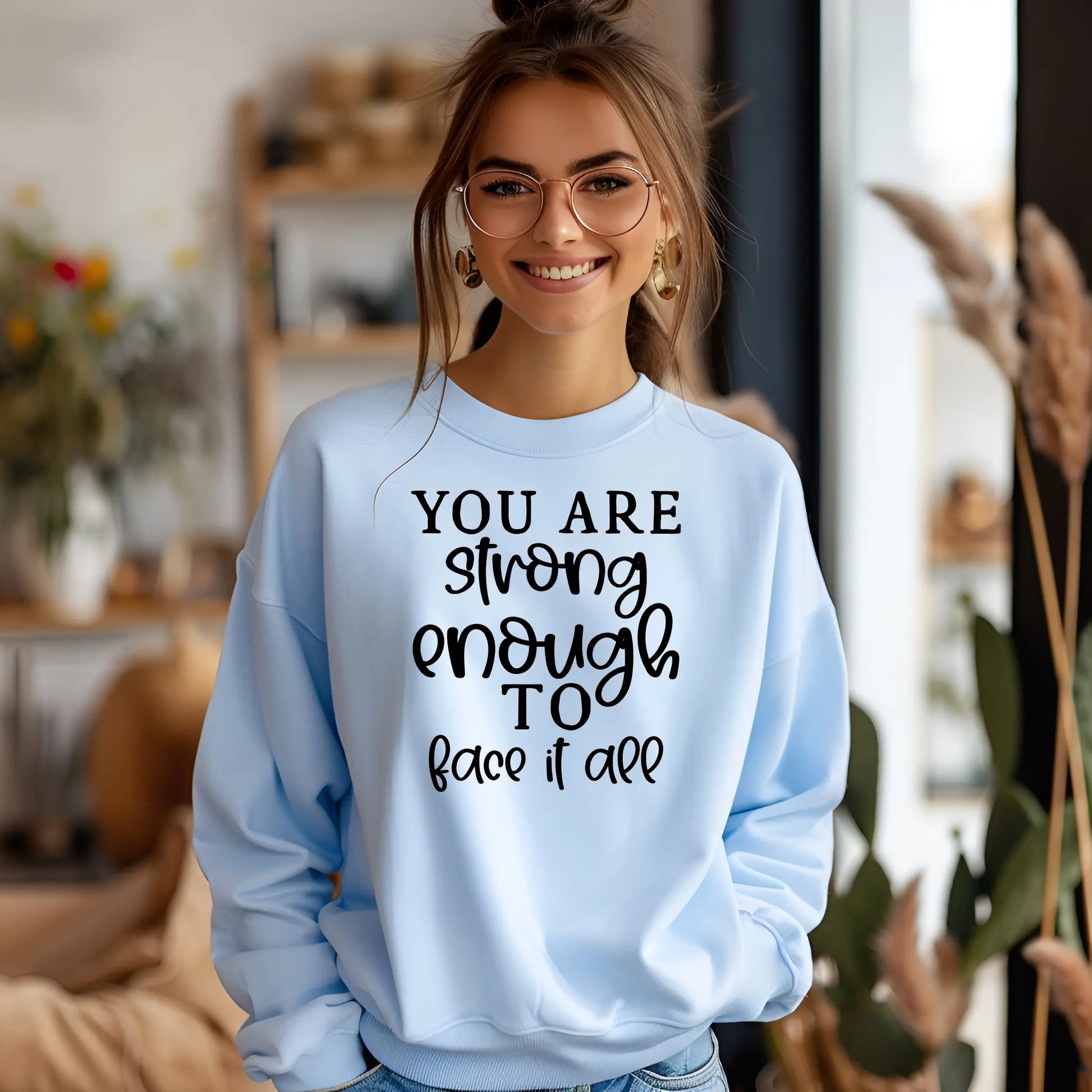 Woman wearing a light blue sweatshirt with motivational text in a home setting