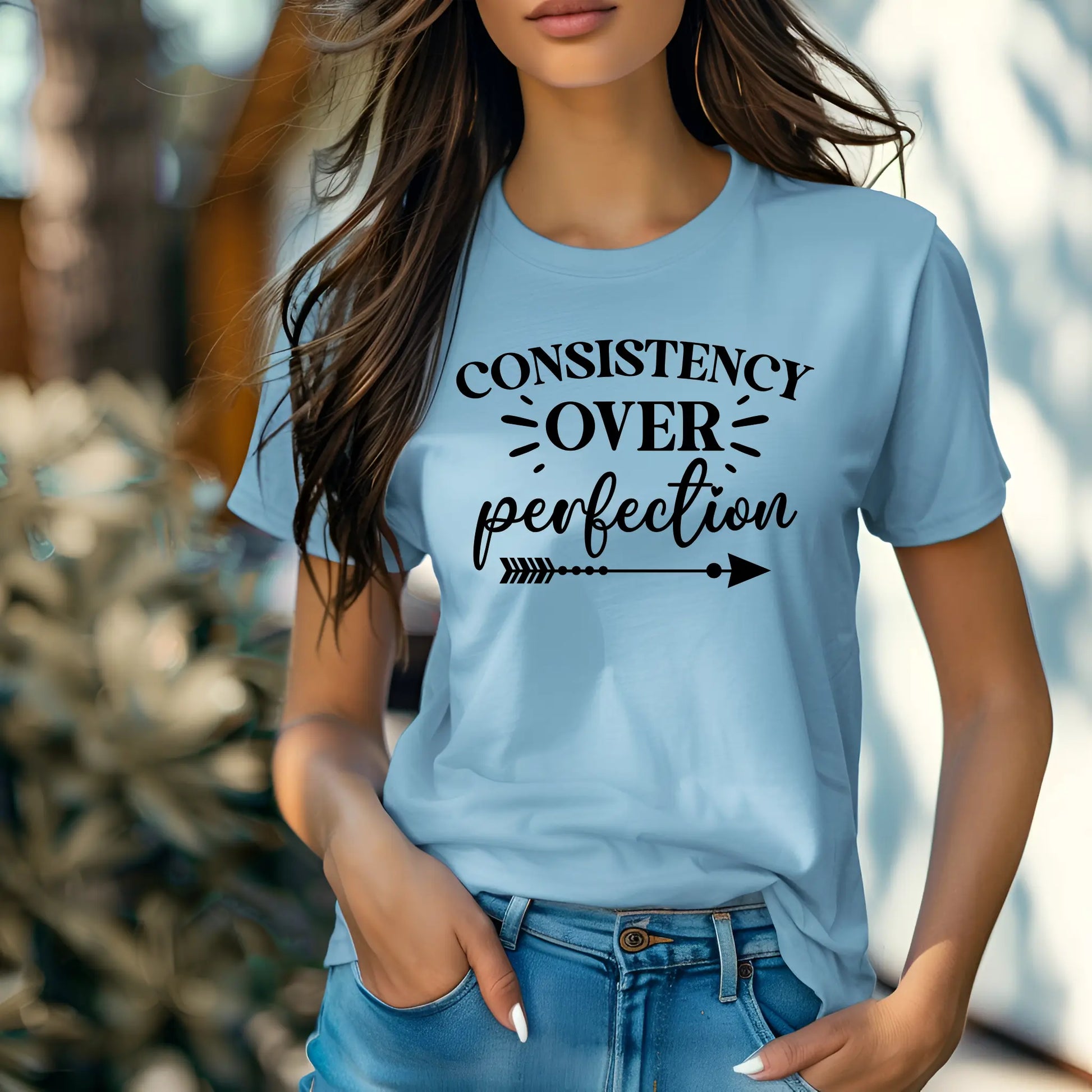 Person wearing a light blue t-shirt with 'Consistency Over Perfection' text.