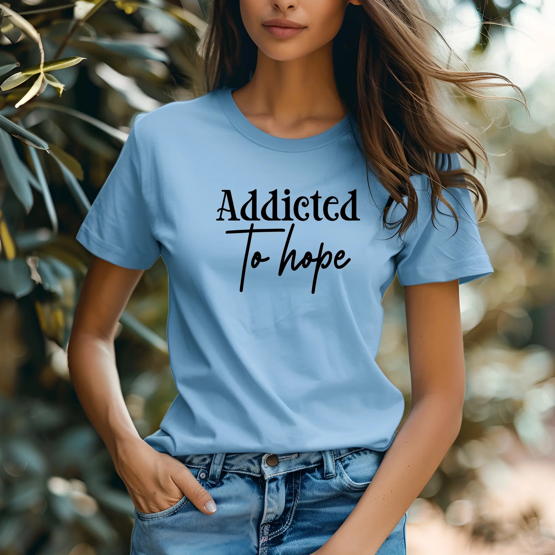 Person wearing a light blue t-shirt with 'Addicted To hope' text in a natural setting
