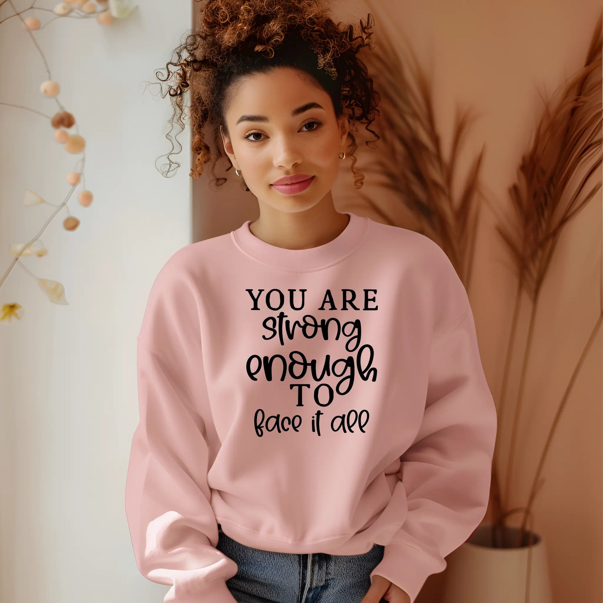 Person wearing a pink sweatshirt with motivational text, standing against a neutral background