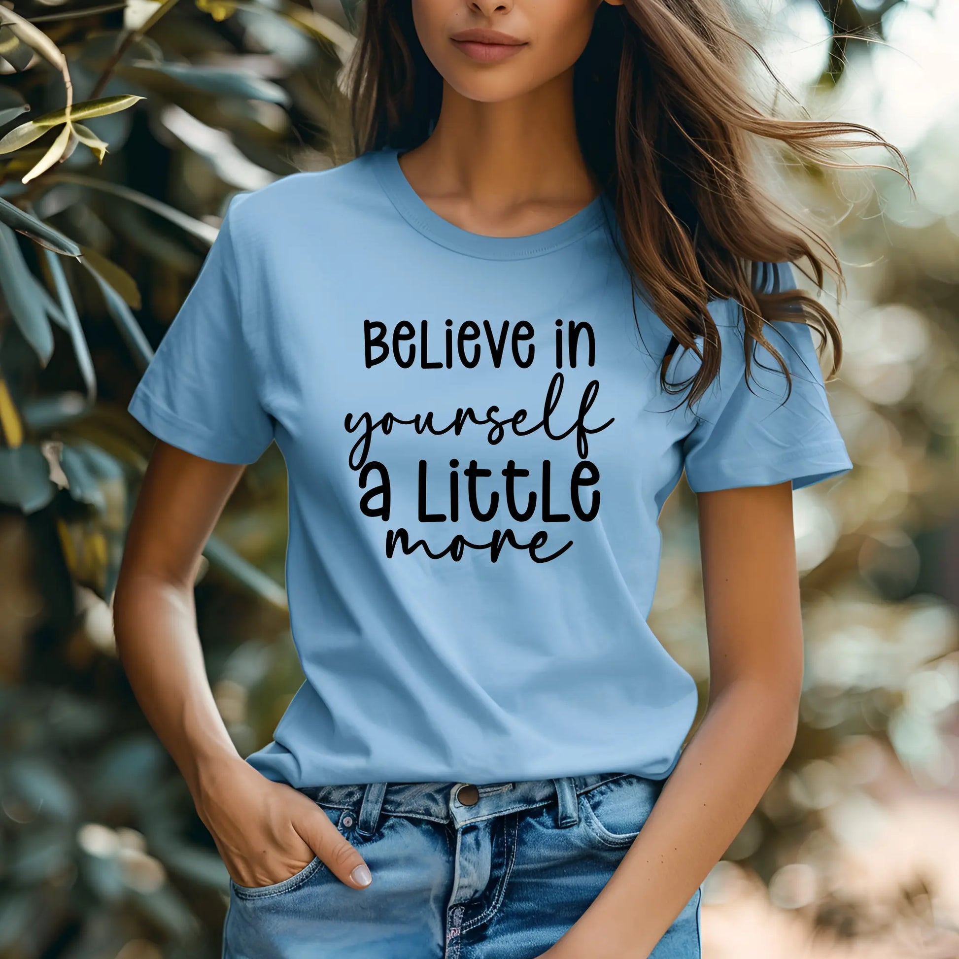 Person wearing a light blue t-shirt with 'Believe in yourself a little more' text, standing outdoors.