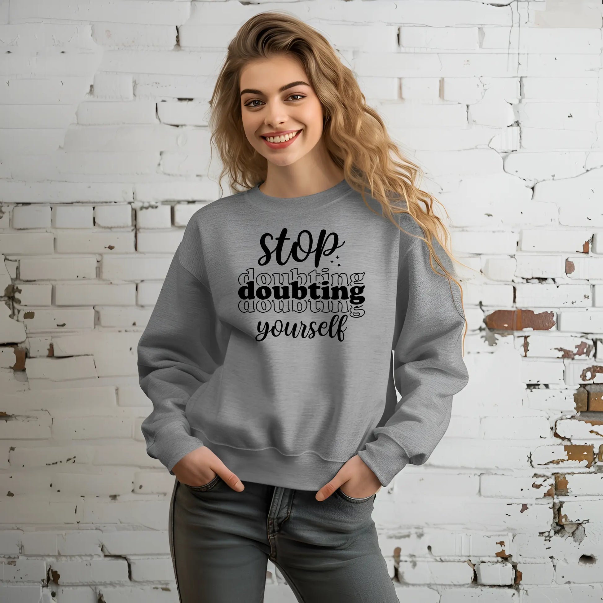 Woman wearing a gray sweatshirt with motivational text against a white brick wall.