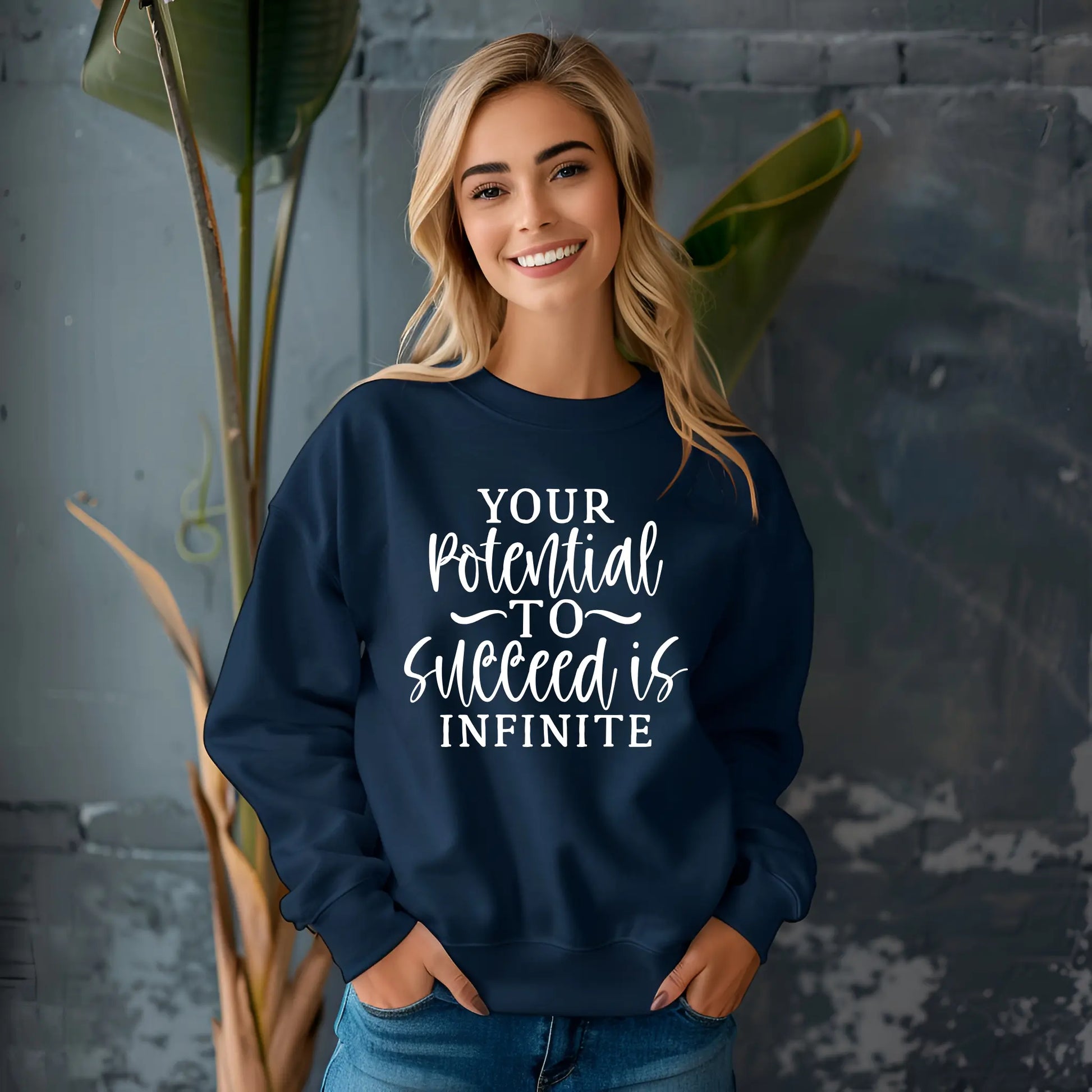 Woman wearing a navy blue sweatshirt with motivational quote, standing against a gray wall with plants.