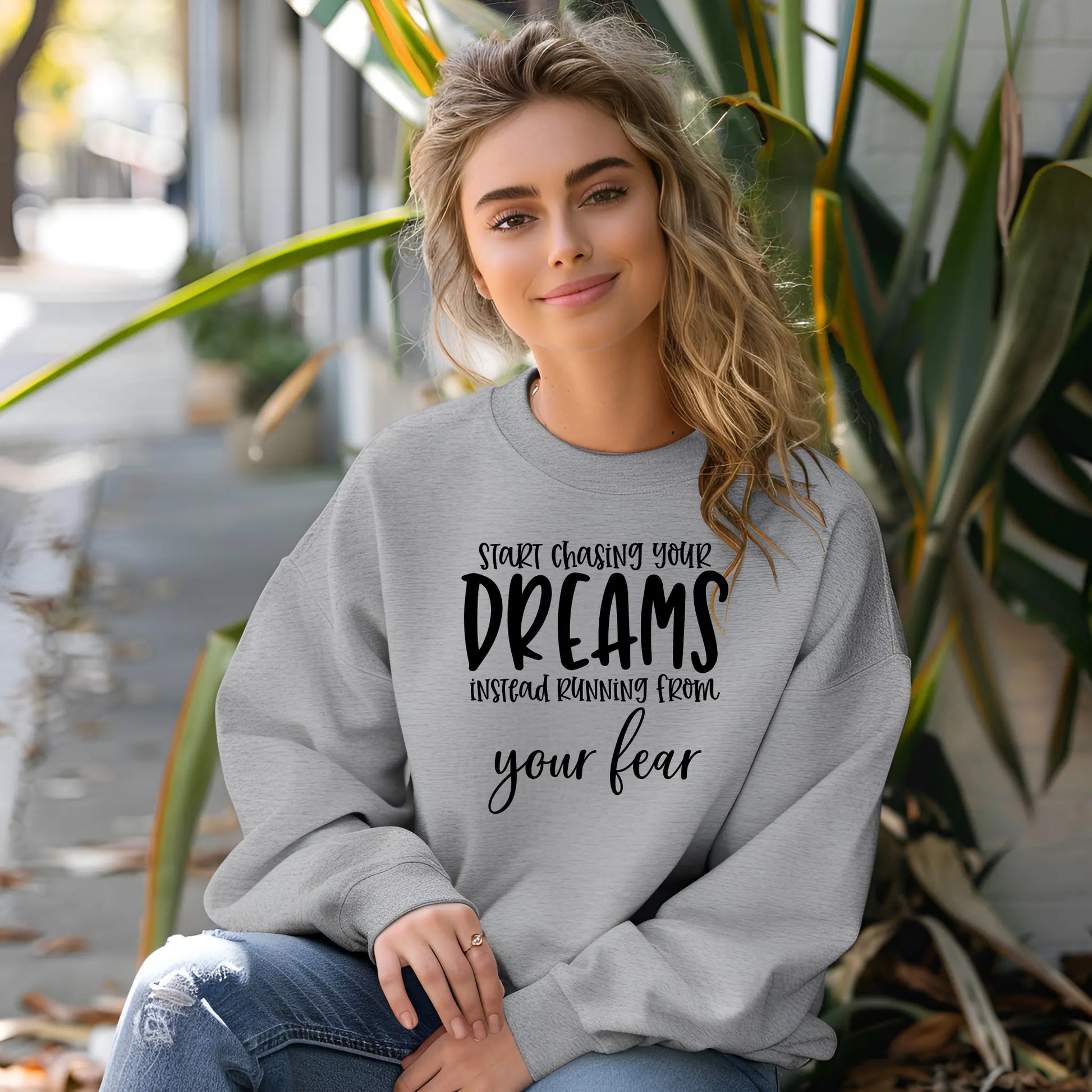 Woman wearing a gray sweatshirt with motivational text, sitting outdoors.