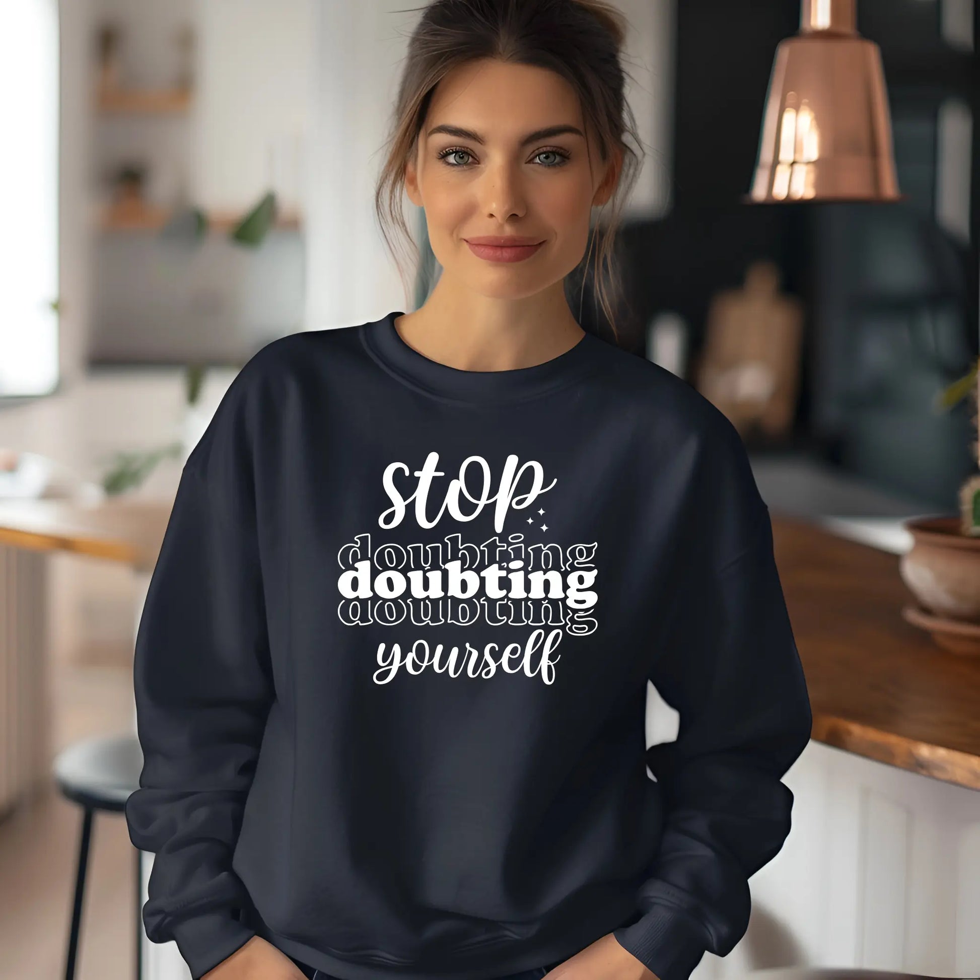 Woman wearing a navy sweatshirt with motivational text in a kitchen setting