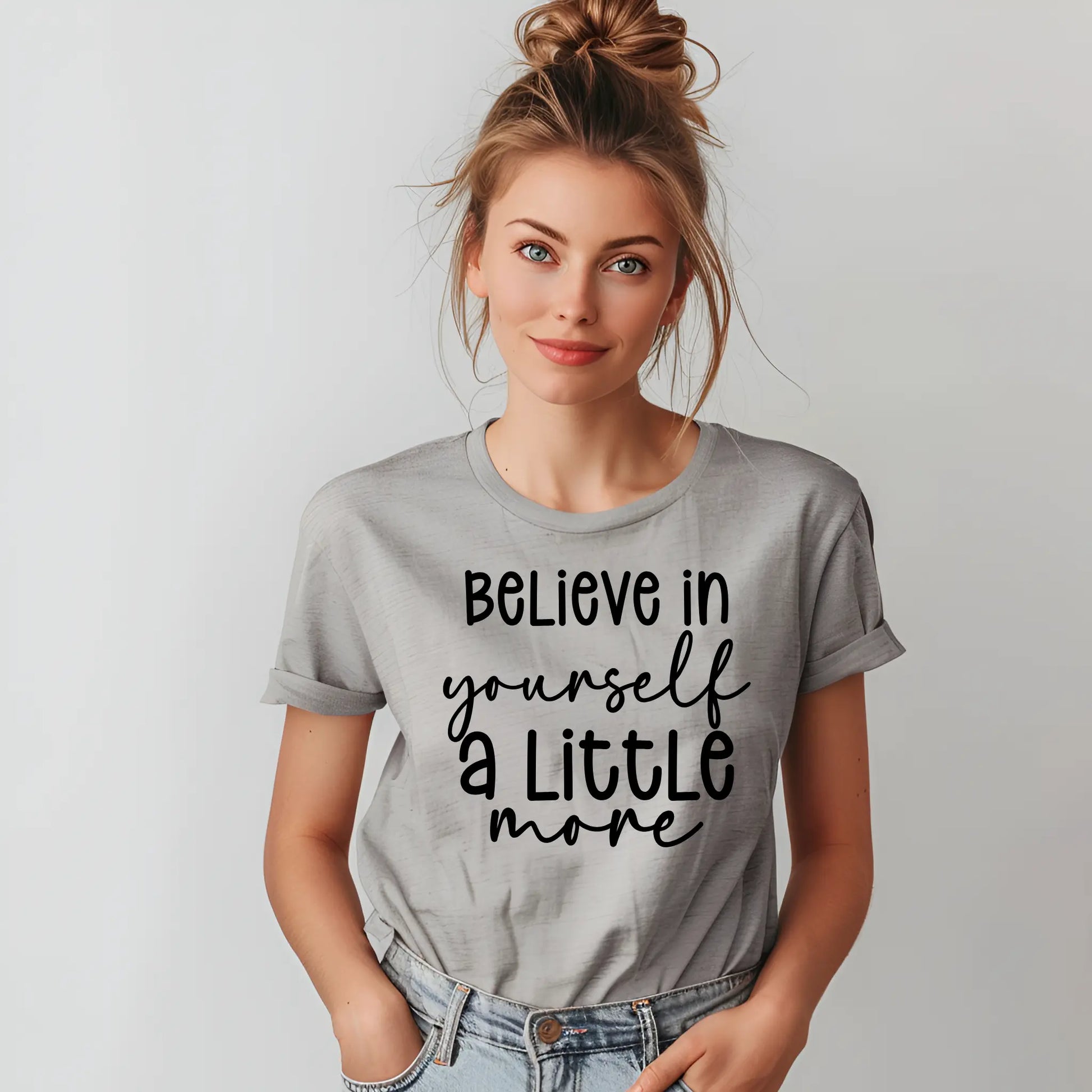 Woman wearing a gray t-shirt with 'Believe in yourself a little more' text on a plain background