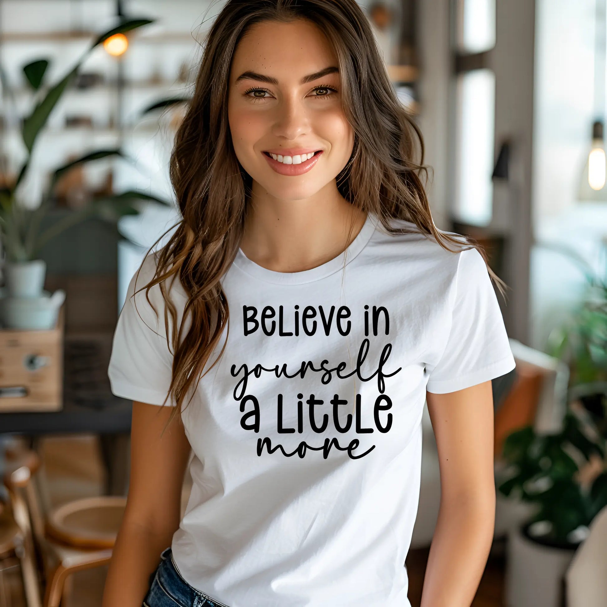 Woman wearing a white t-shirt with 'Believe in yourself a little more' text in a casual indoor setting.