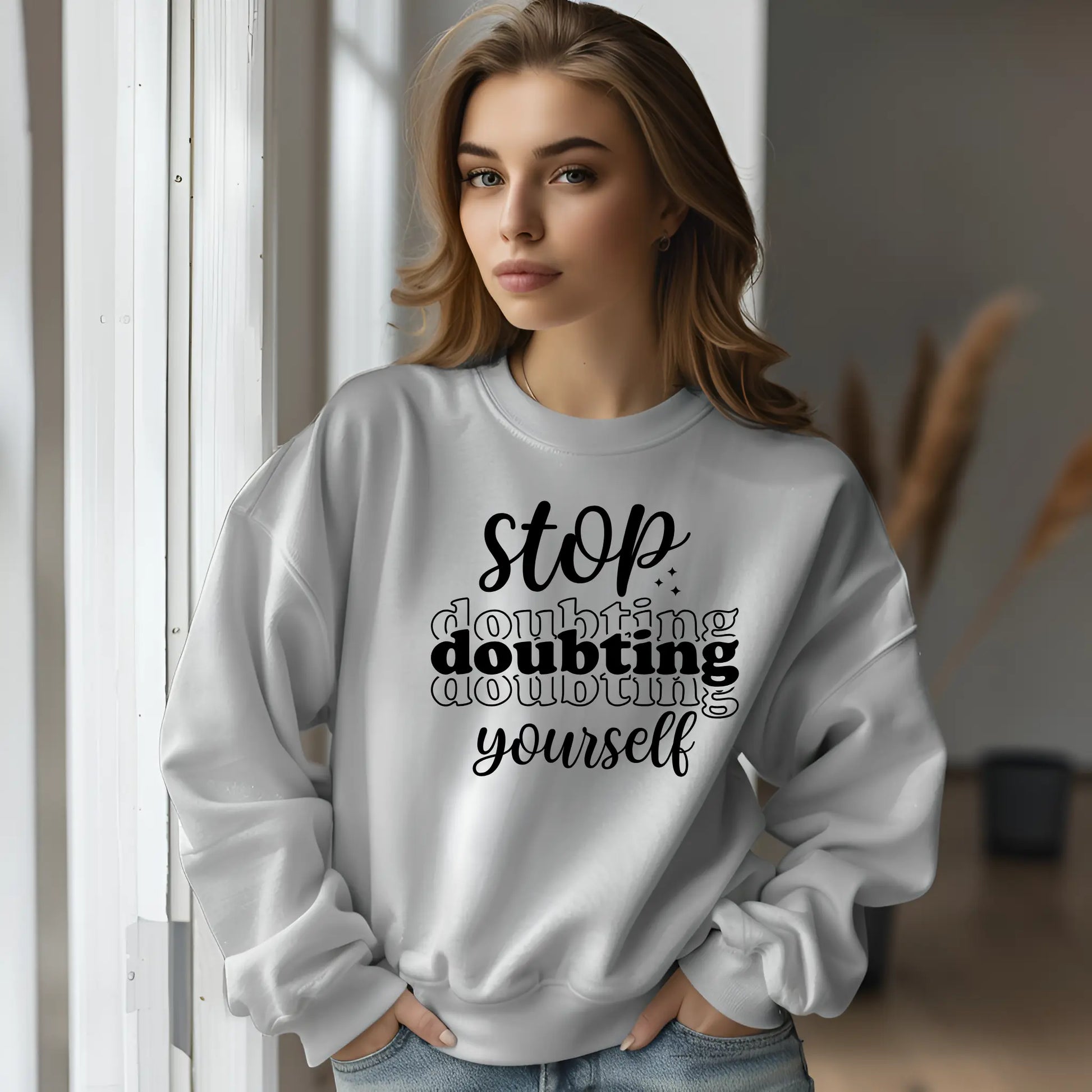 Woman wearing a white sweatshirt with motivational text, standing indoors.