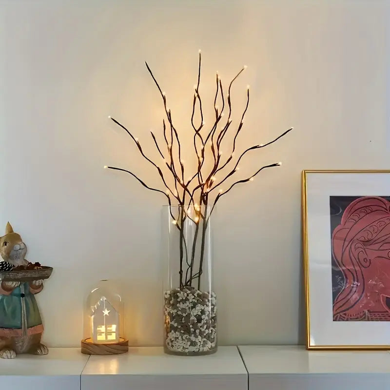 Decorative setup with a vase of lit branches, small figurine, and framed artwork on a shelf.