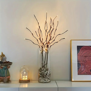 Decorative setup with a vase of lit branches, small figurine, and framed artwork on a shelf.