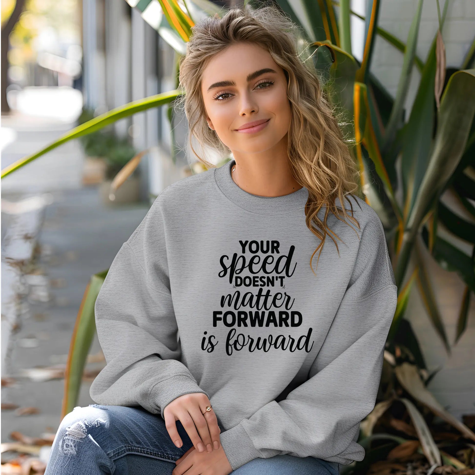 Woman wearing a gray sweatshirt with motivational text, sitting outdoors.